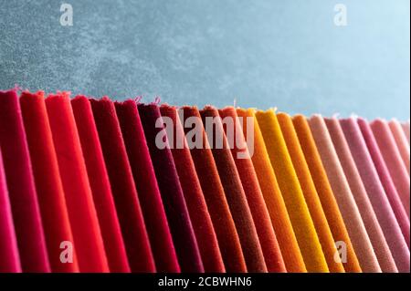 Campioni di velluto morbido in tonalità calde dal rosso all'arancione al rosa posto su un tavolo di pietra scuro in naturale leggero Foto Stock