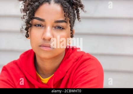 Ragazza adolescente teen femmina giovane Africano americano misto razza biracial donna all'esterno che guarda premuroso e indossa una felpa con cappuccio rossa Foto Stock