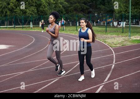 Lezioni di fitness in strada. Le belle amiche corrono sulla pista sportiva dello stadio. Giovani donne in forma atletica. Foto Stock