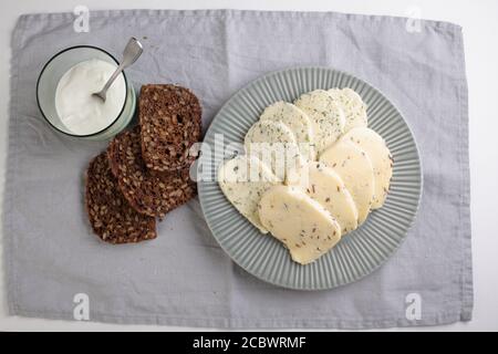 Formaggi estoni con cumino, aneto e aglio, affettati di pane di segale con grani, e una tazza di panna acida Foto Stock