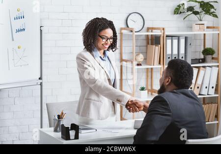 Il manager nero che assume le mani scuotendo con successo candidato vacante dopo il colloquio di lavoro in ufficio, copy space Foto Stock