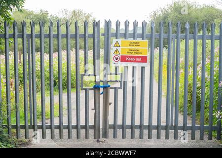 Cancello chiuso con vari avvertimenti di pericolo vicino a un impianto di trattamento delle acque della United Utilities su Red Rock Lane, Stoneclough, Inghilterra, Regno Unito Foto Stock