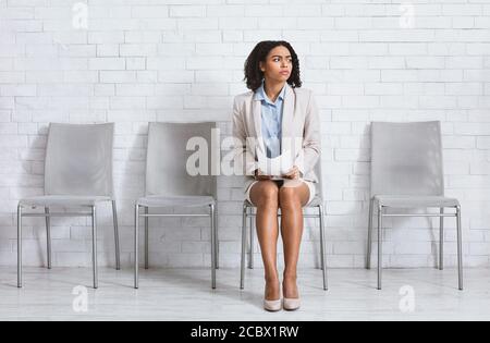 Donna nera preoccupata con CV in attesa di colloquio di lavoro presso la sala dell'azienda, spazio vuoto Foto Stock