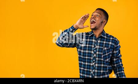 Positivo Black Man gridare tenendo la mano vicino alla bocca, sfondo giallo Foto Stock