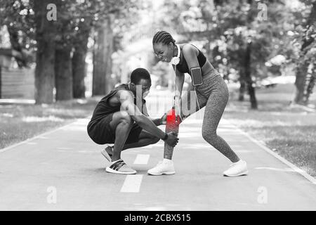 Lesioni alle ginocchia. Donna nera che soffre di trauma durante il jogging con il ragazzo all'aperto Foto Stock