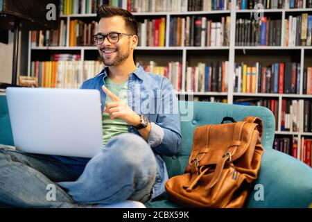 Sorridente studente maschile che lavora e studia in una biblioteca Foto Stock
