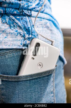la giovane donna ascolta la musica sul suo smartphone bianco attraverso gli auricolari, il telefono si trova nella tasca posteriore dei jeans Foto Stock