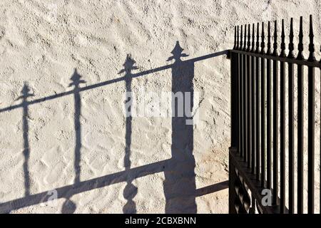 Recinzione in ferro battuto e la sua ombra riflessa sul muro. Foto Stock