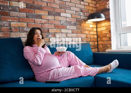 bella donna incinta sta mangiando popcorn mentre guarda il film da sola, si siede sul divano, godere del tempo Foto Stock