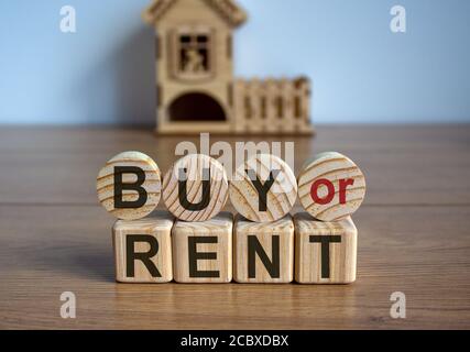 Cubetti e cerchi formano le parole 'buy or rent' di fronte ad una casa in miniatura. Splendido sfondo bianco. Concetto aziendale. Spazio di copia. Foto Stock