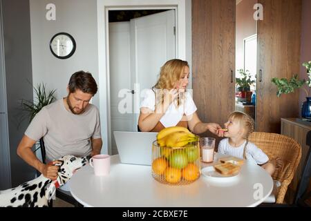 tutte le mattine di felice famiglia caucasica, in cucina, genitori giovani, bambina e adorabile cane dalmata a casa, prima colazione Foto Stock