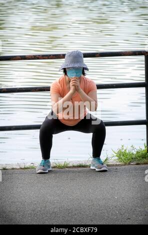 Una donna asiatica americana agile che indossa una maschera si allunga prima di esercitarsi. A Kissena Park, Flushing, New York City. Foto Stock