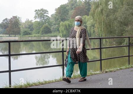 Una donna musulmana che indossa un copricapo e una maschera chirurgica cammina lungo il lago nel Kissena Park, Flushing, New York City Foto Stock