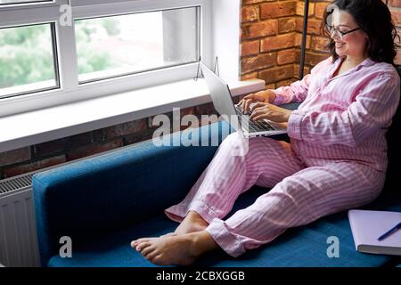 adorabile donna incinta pacifica che lavora con laptop, indossando abiti casalinga. bella brunetta con pancia rotonda su freelance Foto Stock