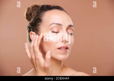 Giovane donna splendida che applica crema facciale o siero su undereye area Foto Stock