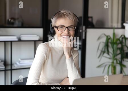 Ritratto di una donna d'affari sorridente dai capelli corti in occhiali e cuffie. Foto Stock