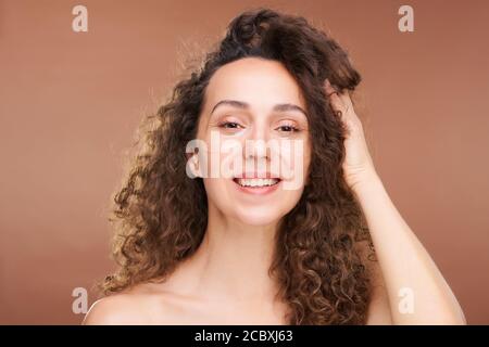 Giovane donna bruna felice con macchie undereye che toccano lungo ondulato capelli Foto Stock