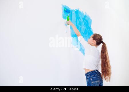 Riparazione nell'appartamento. Bambino felice ragazza dipinge la parete con vernice blu Foto Stock