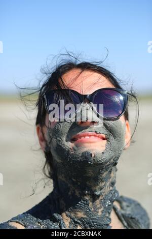 Primo piano ritratto di una giovane donna felice con un fango curativo sul viso. Terapia naturale dell'argilla medicinale Foto Stock