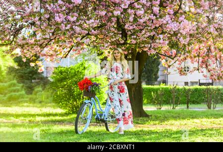 Stagione Sakura. Donna con bouquet di tulipani. Sakura albero in fiore. Giro romantico in bicicletta. Ragazza lungo abito retro Cruiser bicicletta sakura albero. Vacanze di primavera. Concetto di turismo. Trasporto e viaggio. Foto Stock