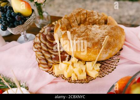 Primo piano di una pagnotta di pane aromatico fresco in un piatto con prosciutto con lardo e formaggio a pasta dura su a. piatto con motivi vicino a una ciotola d'argento con pera e. Foto Stock