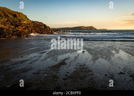 Vista in prima serata della spiaggia di Polzeath con le rocce che riflettono il sole tramontante e i motivi della marea in ritirata. Foto Stock