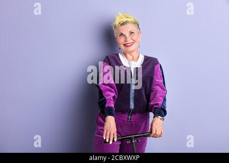 anziana felice fresca donna in bicicletta isolata su sfondo viola. primo piano ritratto, scatto studio. hobby, stile di vita Foto Stock