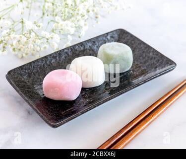 Diversi sapori di Mochi su una piastra rettangolare nera e. Baby Breath Fiori sfondo Blur Foto Stock