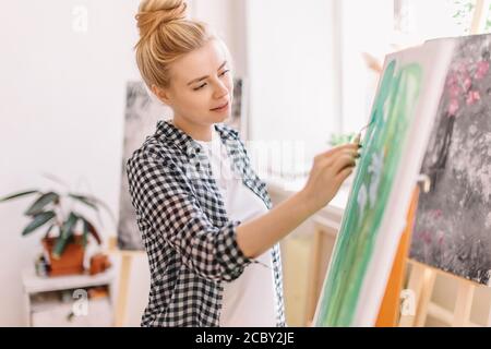 ragazza allegra concentrata sul lavoro con la spatola. primo piano vista laterale foto. strumento necessario per la pittura Foto Stock