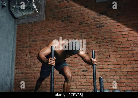 Bodybuilder maschile skinned scuro che esegue peso pesante slitta spingere l'esercizio in cross fit palestra. Foto Stock