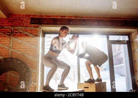 Attività sportive caucasico maschio e femmina sono atleti di eseguire la casella salta in palestra con la polvere e le particelle di gesso galleggianti in aria Foto Stock