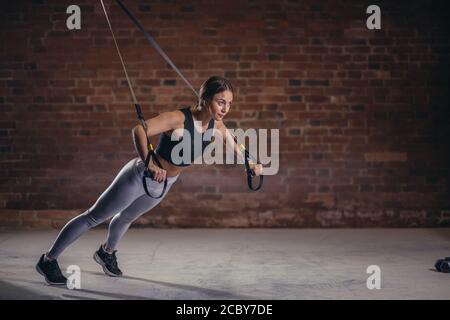 Donna Fitness trainin sul ricetrasmettitore TRX in palestra, facendo spingere ups dove i muscoli di stabilizzazione sono addestrati e tutto il corpo è al lavoro, il che rende tale lavoro Foto Stock