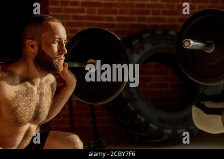 Bel maschio caucasico weightlifter esercizio in palestra, facendo squat esercizio con barbell su apparecchiature crossfit sfondo, vicino. Foto Stock