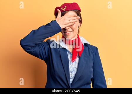 Giovane bella donna che indossa uniforme stewardess sorridente e ridendo con la mano sulla faccia che copre gli occhi per sorpresa. Concetto cieco. Foto Stock