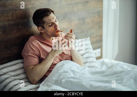 il giovane caucasico prende le droghe a casa da solo. l'uomo conduce uno stile di vita malsano, gli piace fumare marijuana, ganja, cannabis. concetto di medicina della canapa. droghe Foto Stock