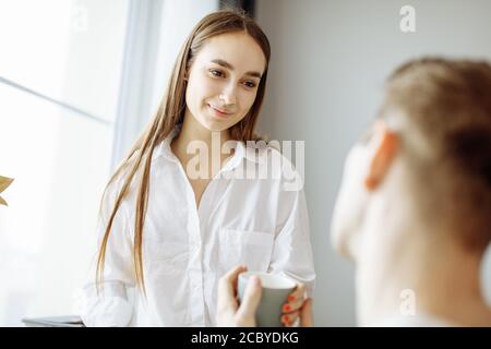 carina signora caucasica parlare bene con il marito al mattino. donna sorridere e guardare l'uomo con amore mentre è seduto sulla sedia. famiglia, relazioni Foto Stock