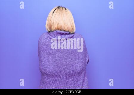 Bella donna bionda Plus taglia indossa un pullover casual turtleneck su sfondo viola abbracciandosi felice e positivo da dietro. Amore di sé Foto Stock