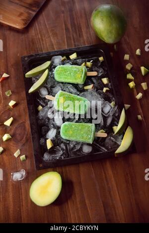 Gelato di mango verde fatto in casa o poppicicles guarnisce con mango pezzi e pezzi di ghiaccio su tavola rustica in legno Foto Stock