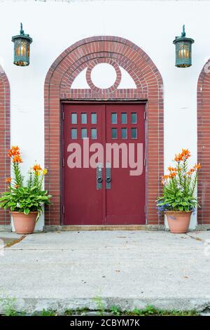 Due alte porte rosse con piccole finestre quadrate sulla parte superiore delle porte in legno e una finestra semicircolare curva sopra l'entrata. Foto Stock