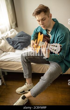 giovane maschio caucasico in abbigliamento casual suonare chitarra acustica a casa, l'uomo eseguire musica, suonare la chitarra nel tempo libero è il suo hobby. musica, concetto hobby Foto Stock