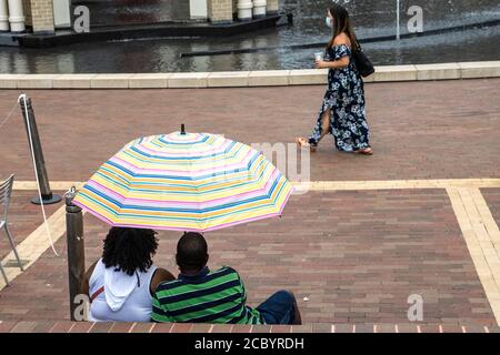 Una coppia riparata sotto un ombrello guarda un passerby. Foto Stock