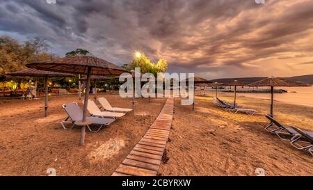 Ombrelloni a canna su vuota spiaggia peleponnese nuvoloso cielo durante colorato tramonto Foto Stock