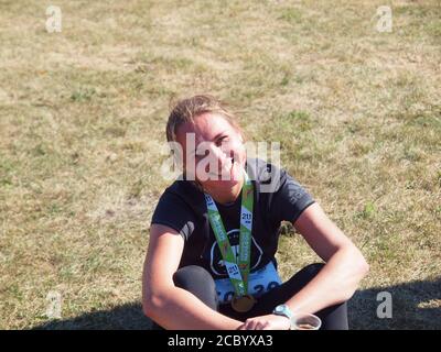 Ritratto di una donna di bellezza con un sorriso perfetto. Corridore seduto in pista con medaglia dopo aver vinto la gara e sorridendo. Foto Stock