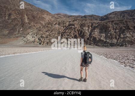 Un escursionista nel bacino di badwater che cammina lungo l'ampio sentiero di ritorno dalla salina verso le montagne nel Parco Nazionale della Valle della morte. Foto Stock