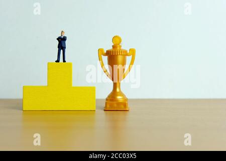 Concetto di business in miniatura - uomo d'affari in piedi su un podio a. ricevi il trofeo d'oro Foto Stock