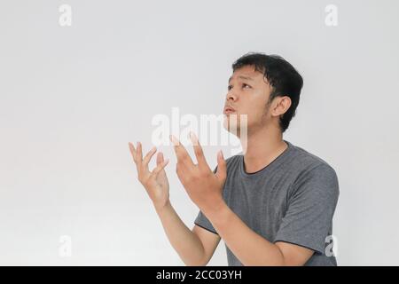 Giovane asiatico in t-shirt grigia pregando con il viso triste Foto Stock