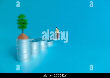 Concetto di business in miniatura - un anziano in piedi su una pila di monete scala per fare gli investimenti finanziari Foto Stock