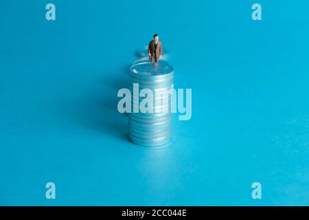 Concetto di business in miniatura - un anziano in piedi su una pila di monete scala per fare gli investimenti finanziari Foto Stock