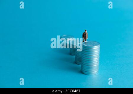 Concetto di business in miniatura - un anziano in piedi su una pila di monete scala per fare gli investimenti finanziari Foto Stock