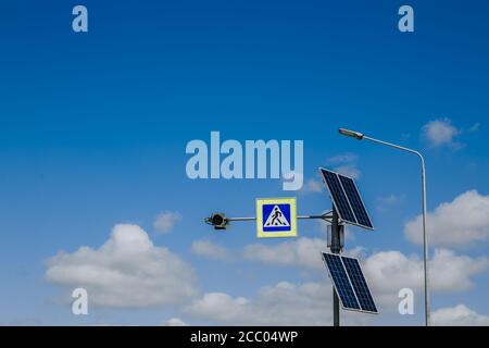 Il cartello di attraversamento pedonale alimentato da pannelli solari installati sopra. Segnaletica stradale e regole. Sullo sfondo di un cielo blu con nuvole Foto Stock